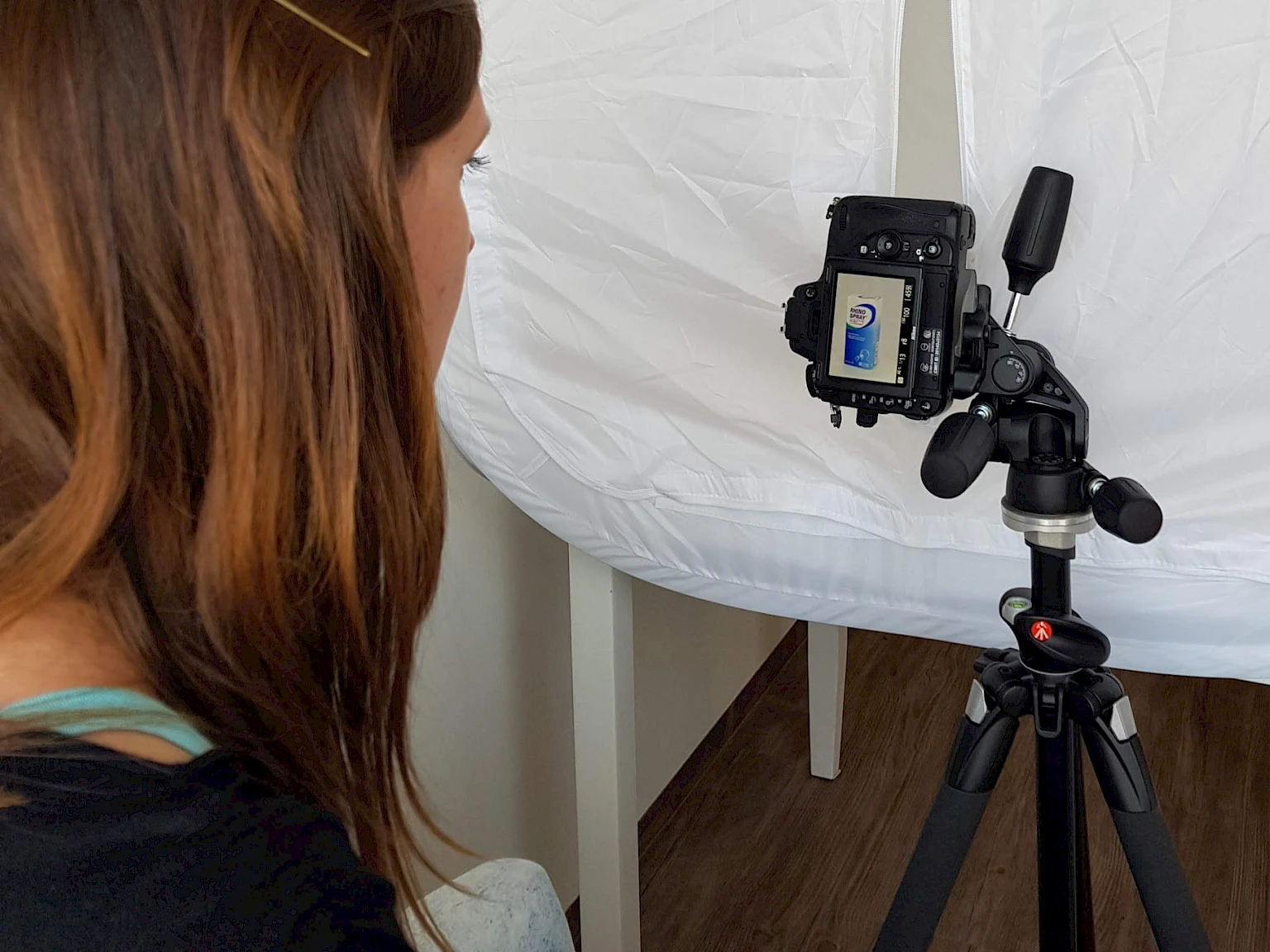 Making-of-Foto bei einem Produktshooting fuer eine Gesundheitskampagne: Eine Fotografin betrachtet das Display einer Kamera auf einem Stativ, auf dem das Produkt Rhinospray Plus zu sehen ist