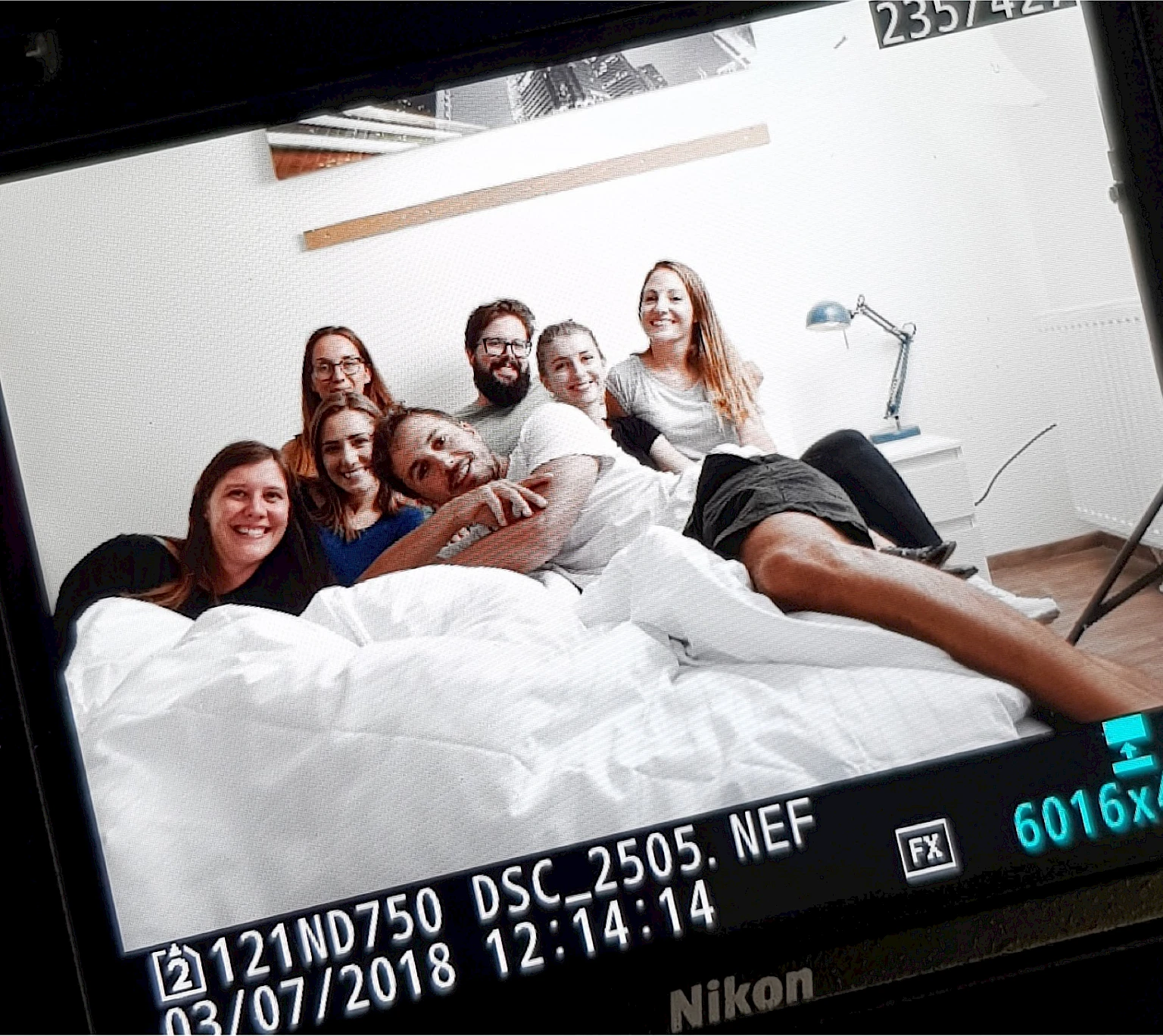 Making-of-Foto direkt vom Kameradisplay: Das gesamte Shooting-Team sitzt und liegt gemeinsam lachend auf einem Bett