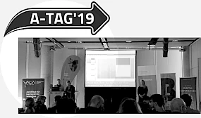 Logo des A-Tags und Ansicht des Praesentationsraums mit Publikum und Buehne.