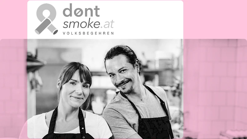 Zwei freundlich lächelnde Menschen in Kochkleidung stehen nebeneinander in einer Küche, darüber das Logo der Initiative dontsmoke.at Volksbegehren