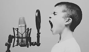 Junge mit geschlossenen Augen, der laut in ein Studiomikrofon schreit