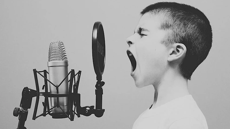 Junge mit geschlossenen Augen, der laut in ein Studiomikrofon schreit