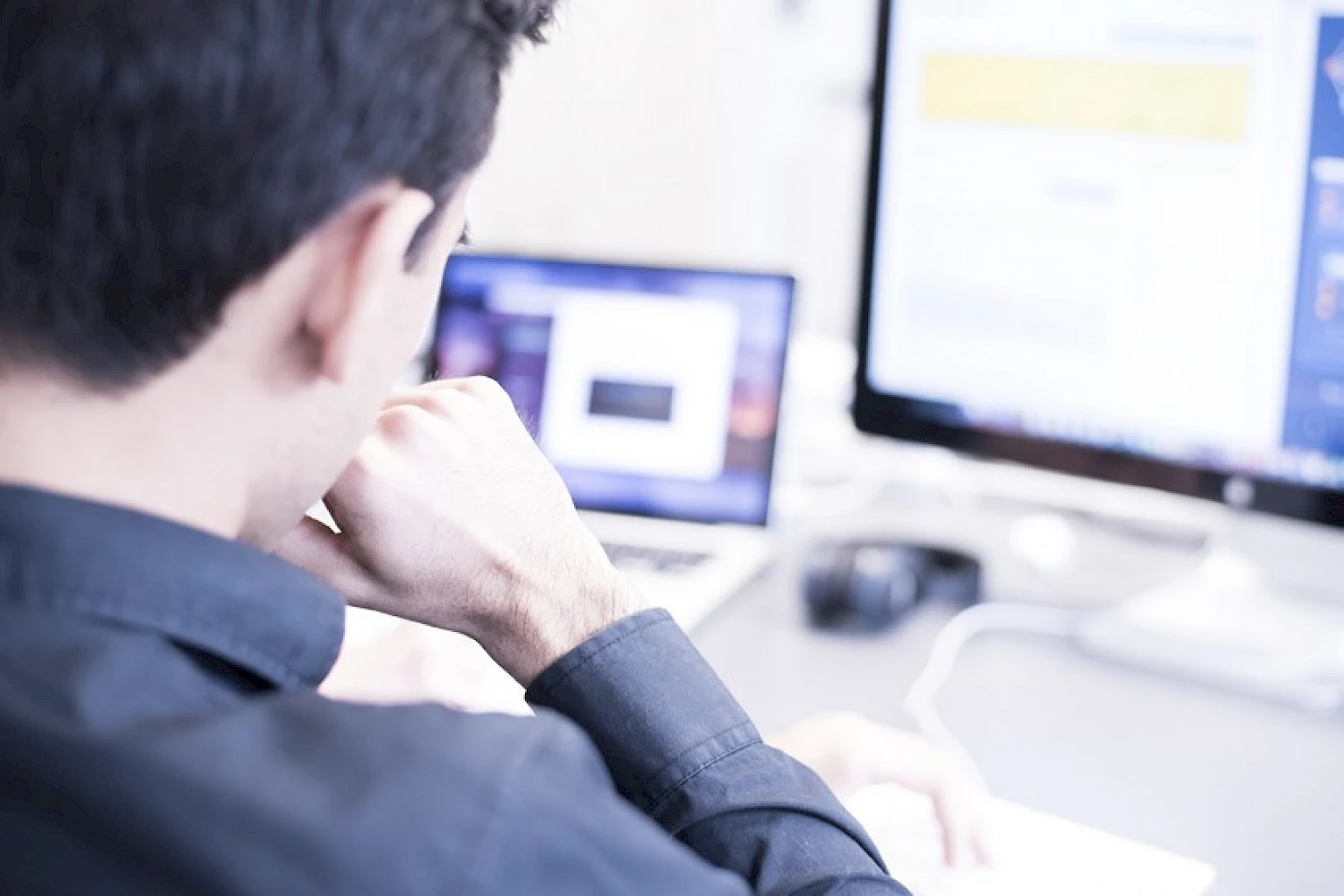 Mann arbeitet konzentriert am Computer mit zwei Bildschirmen in einem modernen Buero