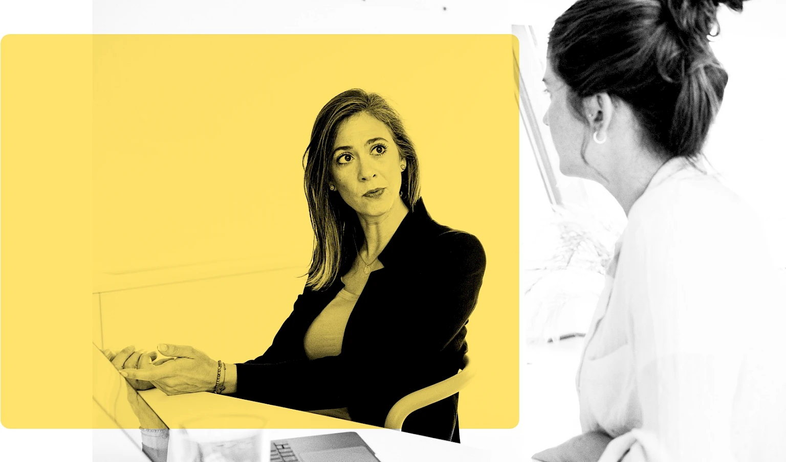 Zwei junge Frauen im Gespraech ueber Arbeitsbedingungen mit offenem Laptop am Tisch