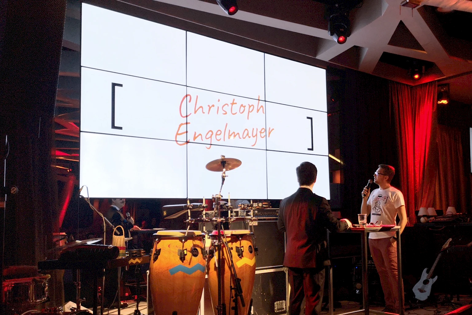 Preisverleihung mit Praesentation des Namens Christoph Engelmayer auf großer Leinwand mit Live-Moderation und musikalischem Setup