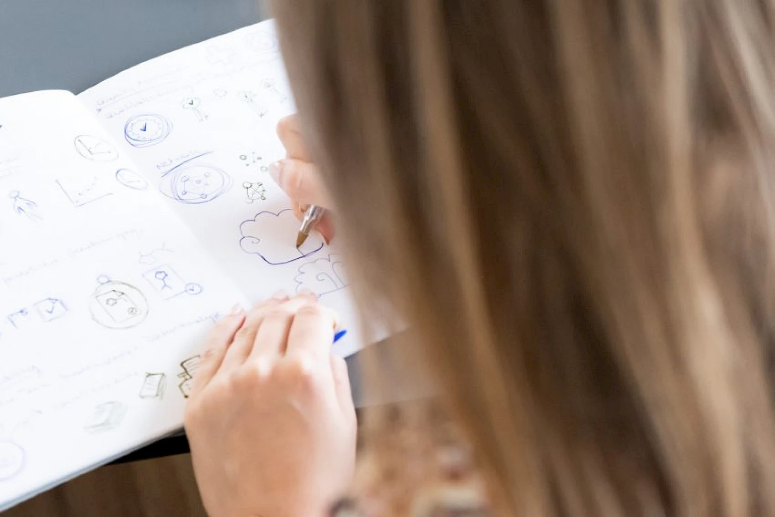 Blick ueber die Schulter einer Frau, die Skizzen in ein Notizbuch zeichnet