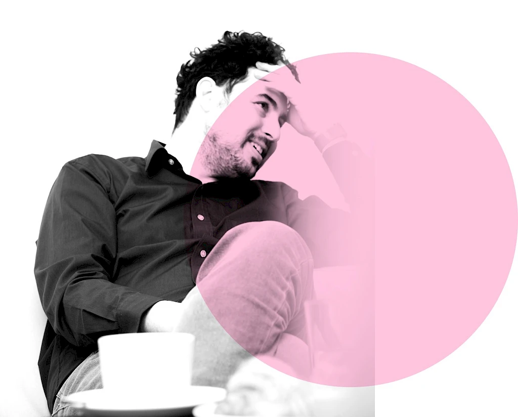 Man sitting on a sofa with one hand on his forehead, contributing to a discussion about rare diseases. A cup is visible on a table in the foreground.